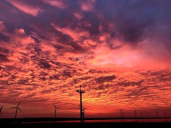 Silhouette windmills on land against dramatic sky during sunset