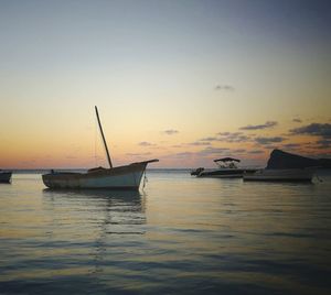 Sailboats moored on sea against sky during sunset