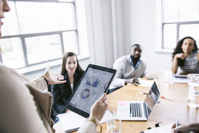 Businesswoman explaining data from tablet computer to colleagues in meeting