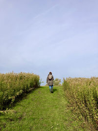 Rear view of woman walking on field against sky