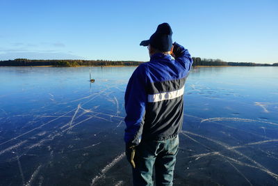 Rear view of senior man standing by lake against clear blue sky