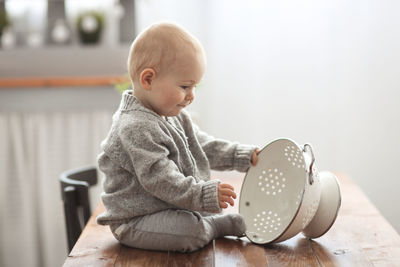 Baby of 10 months plays on the table in the kitchen with kitchen utensils, the concept 