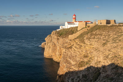 Lighthouse on beach by sea against sky