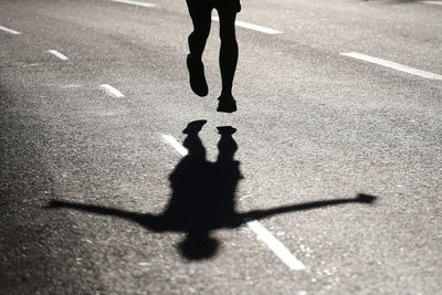 Low section of silhouette man jumping on road during sunny day