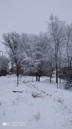 Bare trees on snow covered field against sky