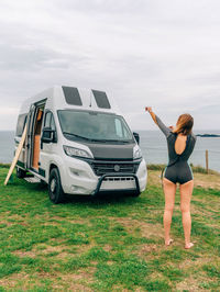 Young woman putting on her wetsuit for surfing next to her camper van