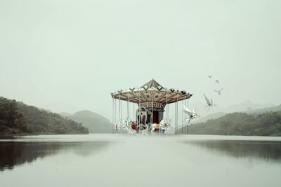 Digital composite of carousel horses flying over lake against clear sky