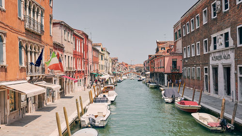 Boats moored in canal amidst buildings against clear sky