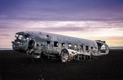 Abandoned car on road against cloudy sky