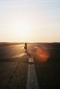 Man riding bicycle on road against sky during sunset