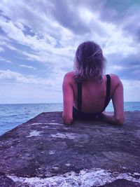 Rear view of mid adult woman relaxing at beach against cloudy sky