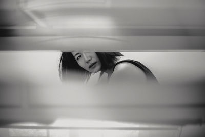 Portrait of mid adult woman sitting in bathroom seen through window blinds