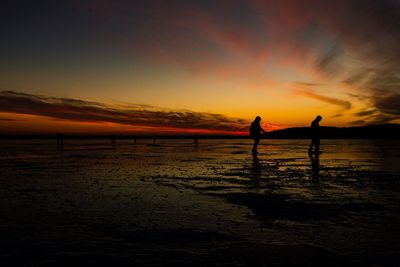 Silhouette people at beach against sky during sunset