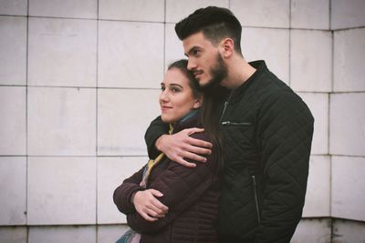 Young couple embracing from behind while standing against wall