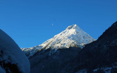 Low angle view of snowcapped mountains against clear blue sky