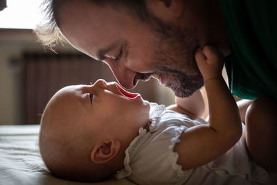 Side view of father face watching his newborn baby in white top laying on the bed