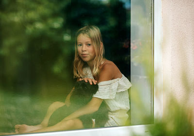 Portrait of young woman sitting on window