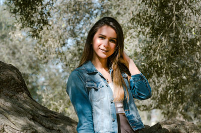 Portrait of smiling young woman standing against trees