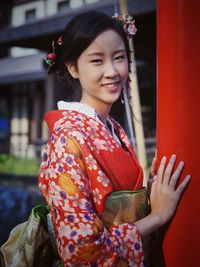 Portrait of smiling teenage girl standing in kimono by red pole