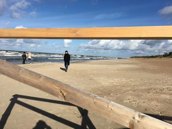 Woman seen through wooden structure against sky at beach