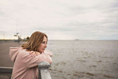 Woman leaning on railing at beach against sky