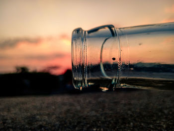 Close-up of glass bottle against sky during sunset