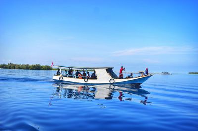 People on boat sailing in sea against blue sky