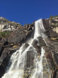 Low angle view of waterfall against clear blue sky