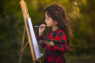 Girl painting on paper over easel at outdoors