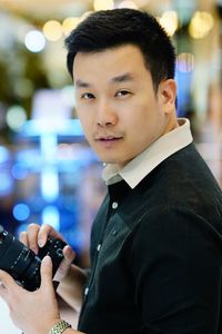 Portrait of man holding camera standing against defocused background