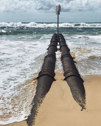 Signboard on concrete pipe at beach against sky