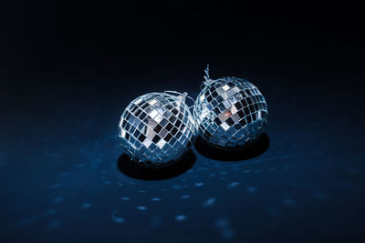 Two mirror balls illuminated by bright light lie on dark blue background with reflections