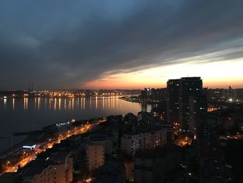 Illuminated cityscape by sea against sky during sunset