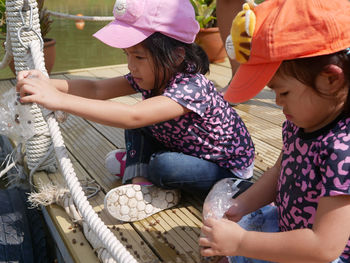 Cute girls wearing cap holding rope sitting on pier by lake