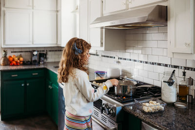 Young girl cooking pretzel dough on stovetop in modern kitchen