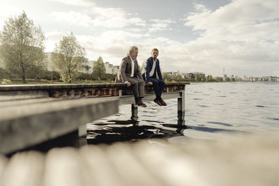 Two businessmen sitting on jetty at a lake