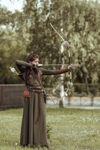 Full length of archer holding bow and arrow standing on field