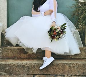 Low section of bride holding bouquet while sitting on steps