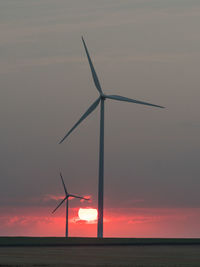 Wind turbines in sea against sky during sunset