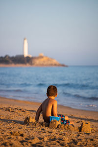 Little kid building castles on the beach. back view