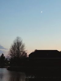 Silhouette bare tree by lake against clear sky at sunset