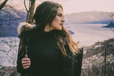 Close-up of young woman standing by bare tree during winter