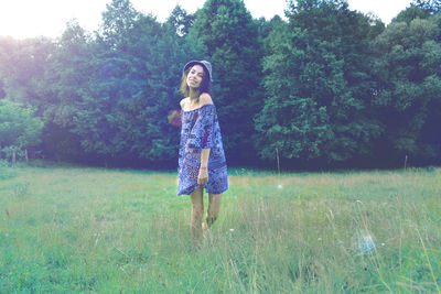 Portrait of young woman standing on field against trees