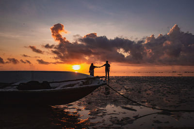 Silhouette people on beach against sky during sunrise