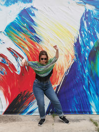 Full length of young woman standing against graffiti wall