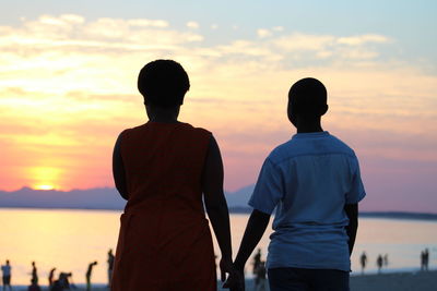 Rear view of silhouette couple standing against sea during sunset