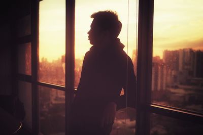 Rear view of silhouette man looking through window