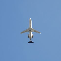 Low angle view of airplane flying against clear blue sky