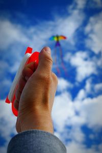 Cropped image of hand flying kite against sky