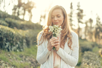 Happy woman with red long hair and a pleasant smile in the rays of the sun holds  flowers 